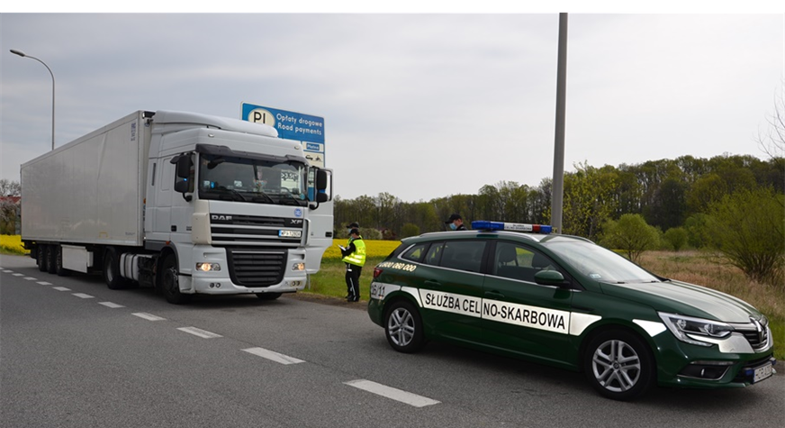 Kontrola drogowa. Funkcjonariusz stoi przy samochodzie ciężarowym, przed ciężarówką stoi radiowóz służby celno-skarbowej.