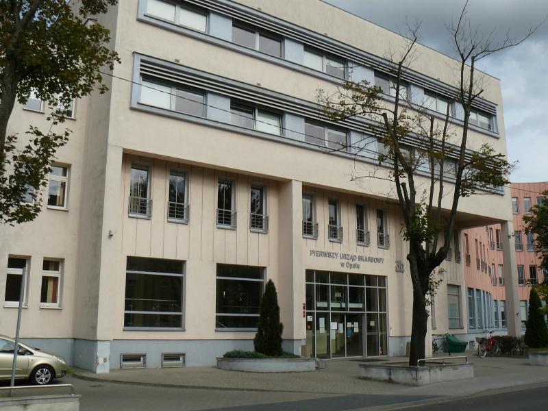 Widok fasady budynku urzędu z oknami i przeszklonym wejściem.Przed budynkiem rosnące drzewa.