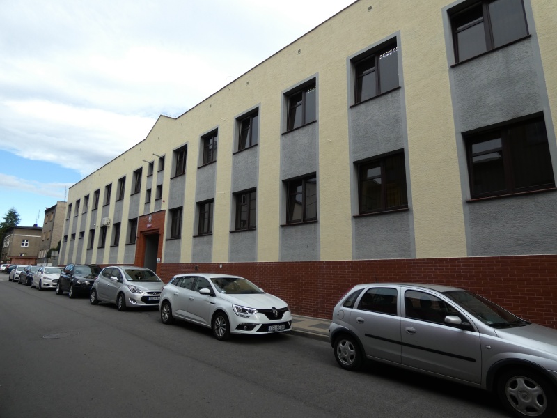 Widok fasady budynku urzedu z oknami i wejsciem.Przed budynkiem na ulicy stoją samochody osobowe.