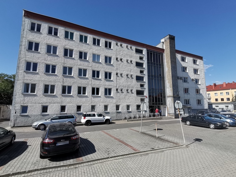 Widok fasady budynku urzędu z oknami.Przed budynkiem ulica i parking ze stojacymi samochodami osobowymi.