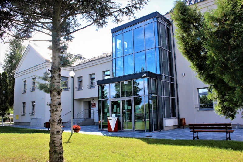Widok fasady budynku Urzędu Skarbowego w Namysłowie.Przeszklone wejście do budynku.Przed budynkiem chodnik oraz trawnik z drzewami.