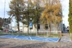 Parking nowej siedziby Urzędu Skarbowego w Namysłowie. Zaznaczone białą kopertą z niebieskim wypełnieniem miejsca dla osób niepełnosprawnych. Parking jest odgrodzony metalowymi barierkami i drzewami.