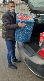 pracownik urzędu skarbowego w Namysłowie z stoi przed otwartym bagażnikiem samochodu, na rękach trzyma prezenty