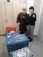 dwie pracownice urzędu skarbowego w Namysłowie stoją przed opakowanymi świątecznym papierem pudłami z prezentami, jedna trzyma uniesiony do góry kciuk lewej dłoni