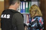 dwóch pracowników opolskiej Krajowej Administracji Skarbowej, mężczyzna w kamizelce z napisem KAS i kobieta stoją tyłem przed szafą z segregatorami, w dłoniach trzymają dokumenty.