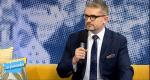 zdjęcie: w studio telewizyjnym siedzi na kanapie pracownik urzędu skarbowego, w lewej dłoni trzyma mikrofon
