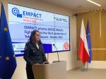 Szef KAS Magdalena Rzeczkowska stoi przed mównicą, za nią ekran elektroniczny wyświetlający nazwę konferencji EMPACT, po bokach mównicy flagi Polski i Unii Europejskiej