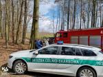 na drodze leśnej stoi radiowóz Służby Celno-Skarbowej, a za nim samochód gaśniczy Straży Pożarnej. Za radiowozem stoi funkcjonariusz Służby Celno-Skarbowej oraz dwóch mężczyzn