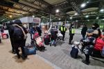 terminal przejścia granicznego, kobiety z dziećmi w wózkach, z walizkami, funkcjonariusz Policji prowadzi kobietę na wózku inwalidzkim.