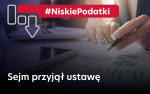 Napis NiskiePodatki. Sejm przyjął ustawę oraz dłoń z długopisem