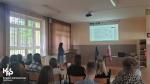 pracownica Urzędu Skarbowego stroi przed klasą, uczniowie siedzą na krzesłach, na ekranie jest wyświetlona prezentacja, 