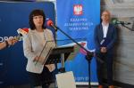 Dyrektor IAS w Opolu stoi przy mównicy, za  nią stoi męzczyzna.