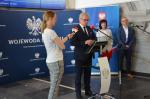 Wojewoda Opolski stoi przy mównicy. Kobieta kieruje mikrofon w jego stronę.W tle baner Urżędu Wojewódzkiego w Opolu. Za nim stoi Dyrektor IAS w Opolu i mężczyzna.