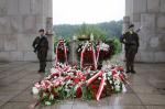 Dwaj żołnierze stoją pod pomnikiem udekorowanym wieńcami.