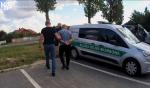 funkcjonariusze Służby Celno-Skarbowej prowadzą zatrzymaną osobę, na rękach ma założone kajdanki. Obok radiowóz Służby Celno-Skarbowej