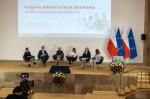 Uczestnicy panelu dyskusyjnego siedzą. W tle prezentacja