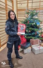 funkcjonariuszka trzyma w dłoniach kartkę z podziękowaniami dla Izby Administracji Skarbowej w Opolu obok przystrojona świątecznie choinka i prezenty