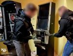 dwóch funkcjonariuszy Służby Celno-Skarbowej za pomocą narzędzi otwiera nielegalny automat do gier hazardowych