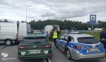 radiowozy Służby Celno-Skarbowej i Policji przed nimi bus z migrantami i funkcjonariusze służb