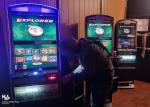 Zdjęcie przedstawia wnętrze nielegalnego salonu do gier. Na pierwszym planie widać pochylonego mężczyznę, który otwiera automat do gier. Za nim stoją w rzędzie trzy automaty do gier.