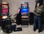 Funkcjonariusze w salonie gier stoją przy automatach do gier
