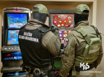 Dwóch funkcjonariuszy KAS stoi przed automatami do gry w nielegalnym salonie gier