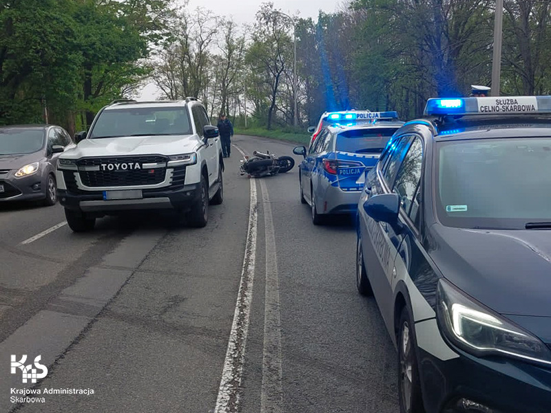 droga w mieście, po obu pasach stoją pojazdy, z lewej strony radiowóz Służby Celno-Skarbowej, pomiędzy pojazdami leży uszkodzony motocykl