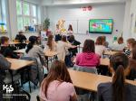 przedstawicielki Urzędu Skarbowego w Kluczborku stoją w klasie szkolnej przy tablicy, uczniowie siedzą w ławkach