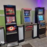 Trzy automaty do gier stoją przy ścianie. Na ekranach automatów widać różnokolorowe obrazy, grafiki, liczby.