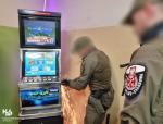 Dwóch funkcjonariuszy stoi przy jednym automacie do gier. Funkcjonariusz próbuje otworzyć automat urządzeniem, z którego lecą iskry.