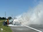 płonący samochód na autostradzie, z maski pojazdu wydobywa się dym, funkcjonariusz KAS gasi pożar gaśnicą