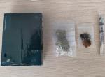 na stole leżą pudełko z kapsułkami, suszona marihuana w małym woreczku strunowym, substancja w małym woreczku strunowym oraz tzw. skręt z marihuany