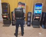 funkcjonariusz Krajowej Administracji Skarbowej w nielegalnym salonie gier stroi przed trzema automatami do gier hazardowych