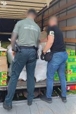 Funkcjonariusz Służby Celno-Skarbowej i Policji zabezpieczają towar. Stoją za otwartą przestrzenią ładunkową pojazdu i analizują zabezpieczony towar.