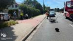 Funkcjonariusze opolskiej Służby Celno-Skarbowej (kobieta i mężczyzna) w oddali pomagają rannemu motocykliście. Funkcjonariusz pochylony nad poszkodowanym. Po lewej stronie funkcjonariusza stoi funkcjonariuszka.