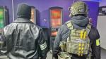 funkcjonariusz Policji i funkcjonariusz Służby Celno-Skarbowej stoją tyłem w pomieszczeniu z automatami do nielegalnych gier hazardowych