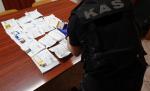 Funkcjonariusz opolskiej KAS nachyla się nad biurkiem na ktorym leżą saszetki z narkotykami